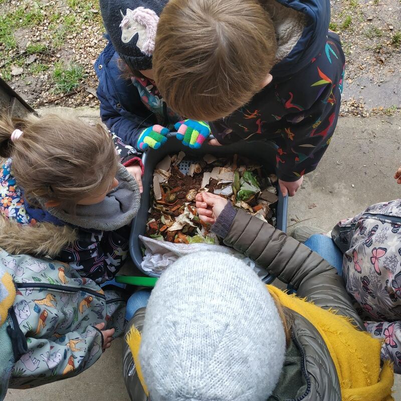 Des enfants penchés sur un bac rempli de feuilles et de terre