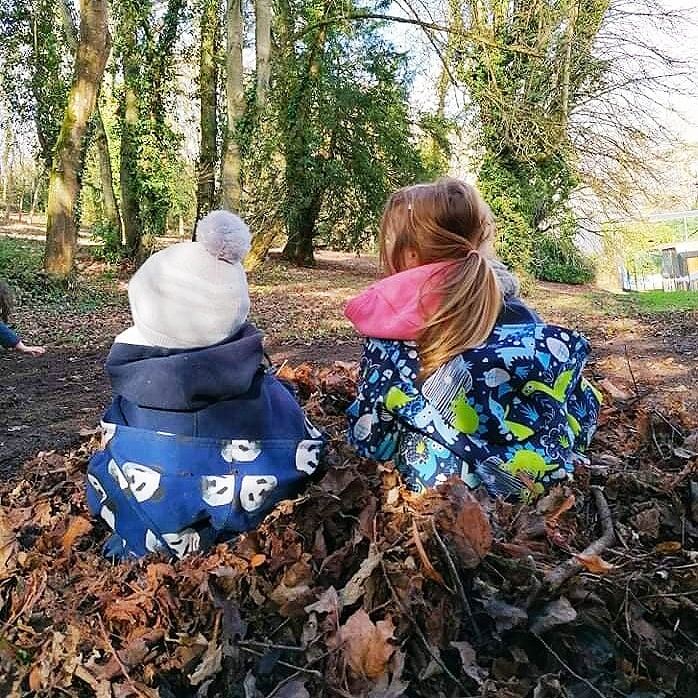 Deux enfants, de dos, assis dans un tas de feuilles