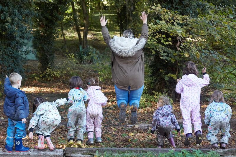 Une éducatrice et des enfants, de dos, sautent ensemble dans le bois de l'école